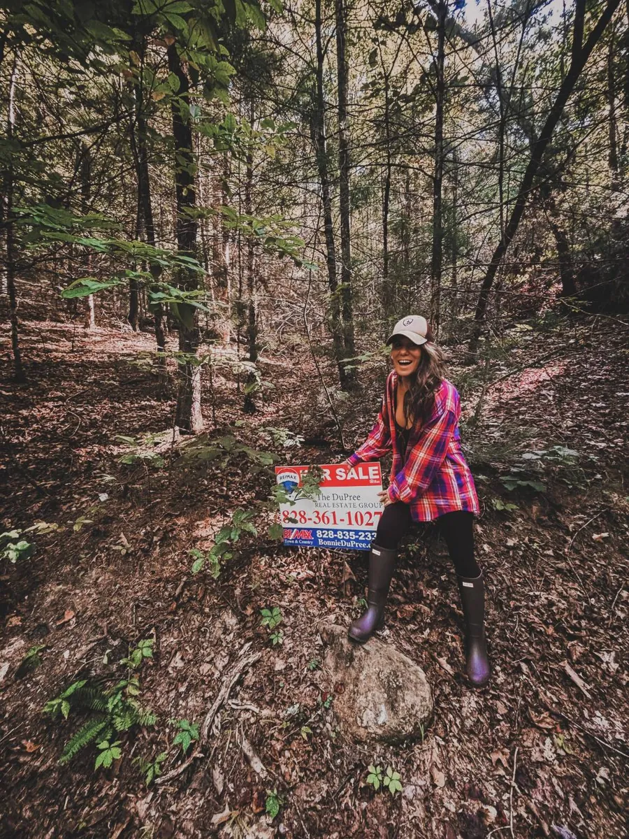 Melodie laughing beside a For Sale sign in the woods